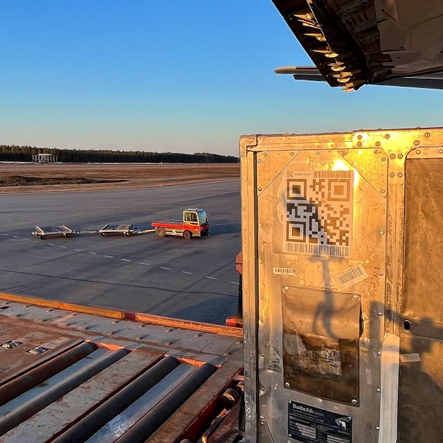 A box is being loaded into a cargo plane. The box has a QR code on a side. The sun is setting.