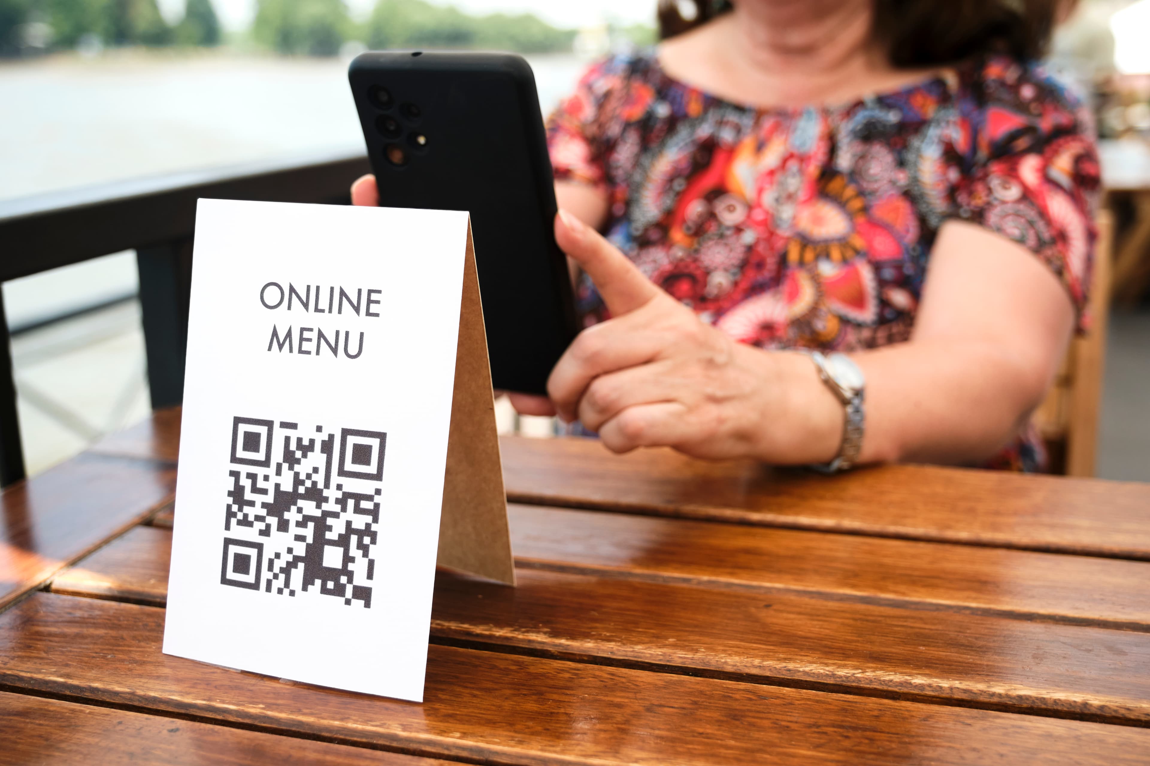 A woman sitting in a restaurant and scanning a QR code menu with her phone. The QR code redirects her to the menu.