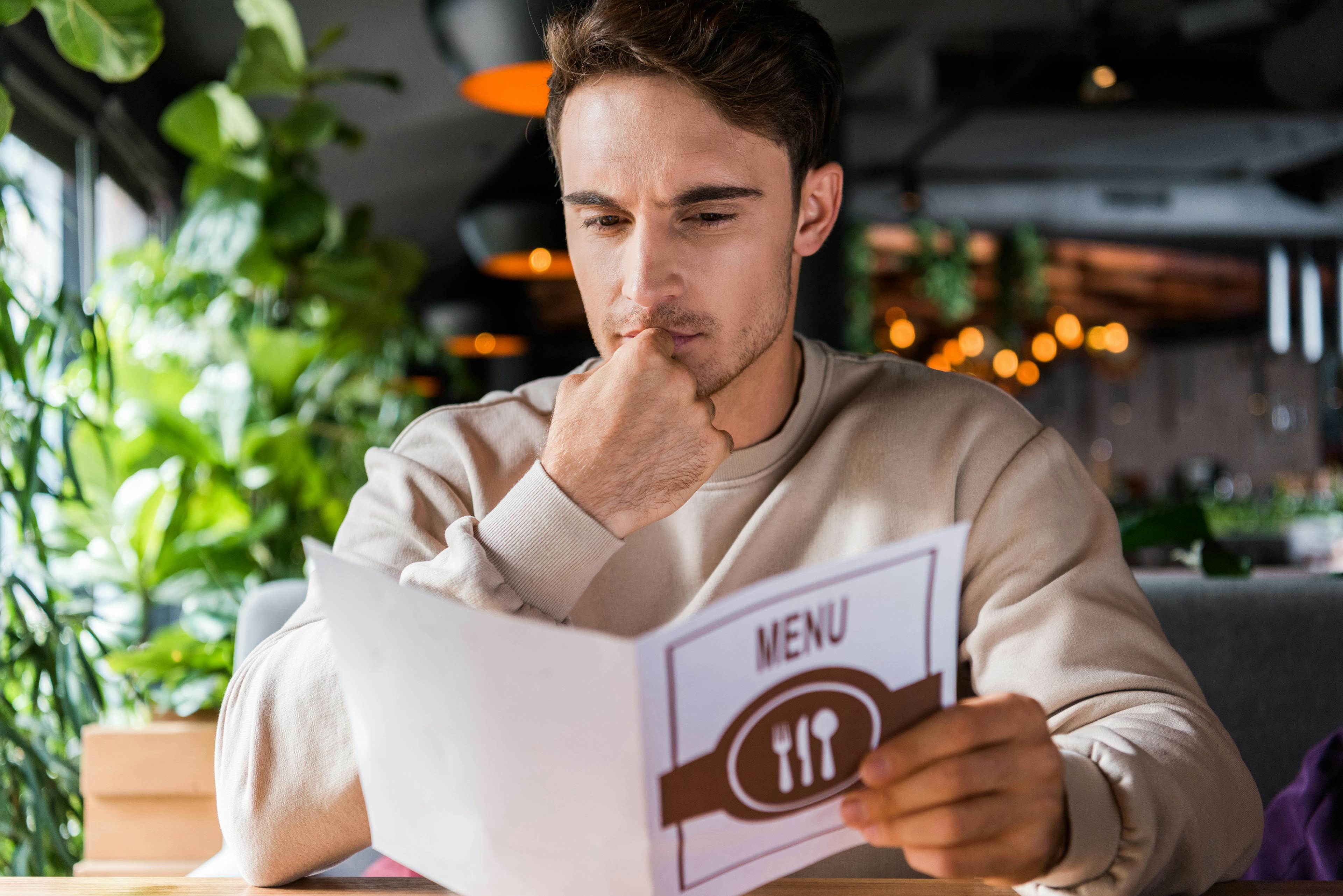 A man is sitting in a restaurant and reading the menu.