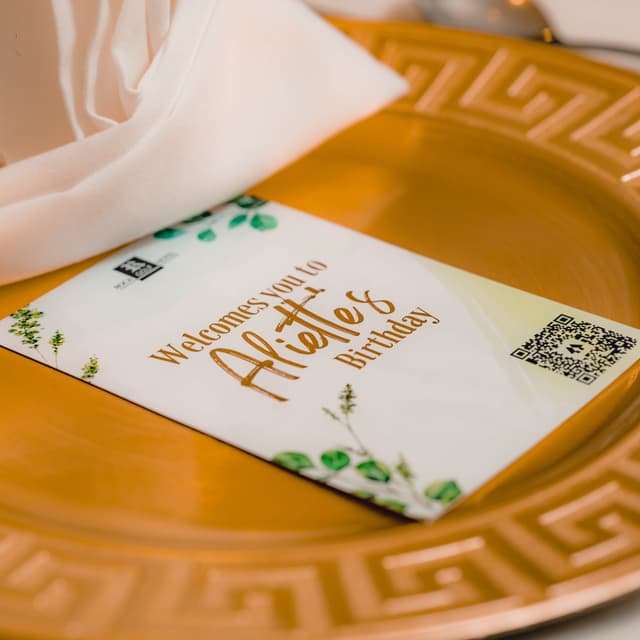 A birthday card is laying on a plate. The QR code is printed on a birthday card. Scanning the code redirects people to the food ordering service.