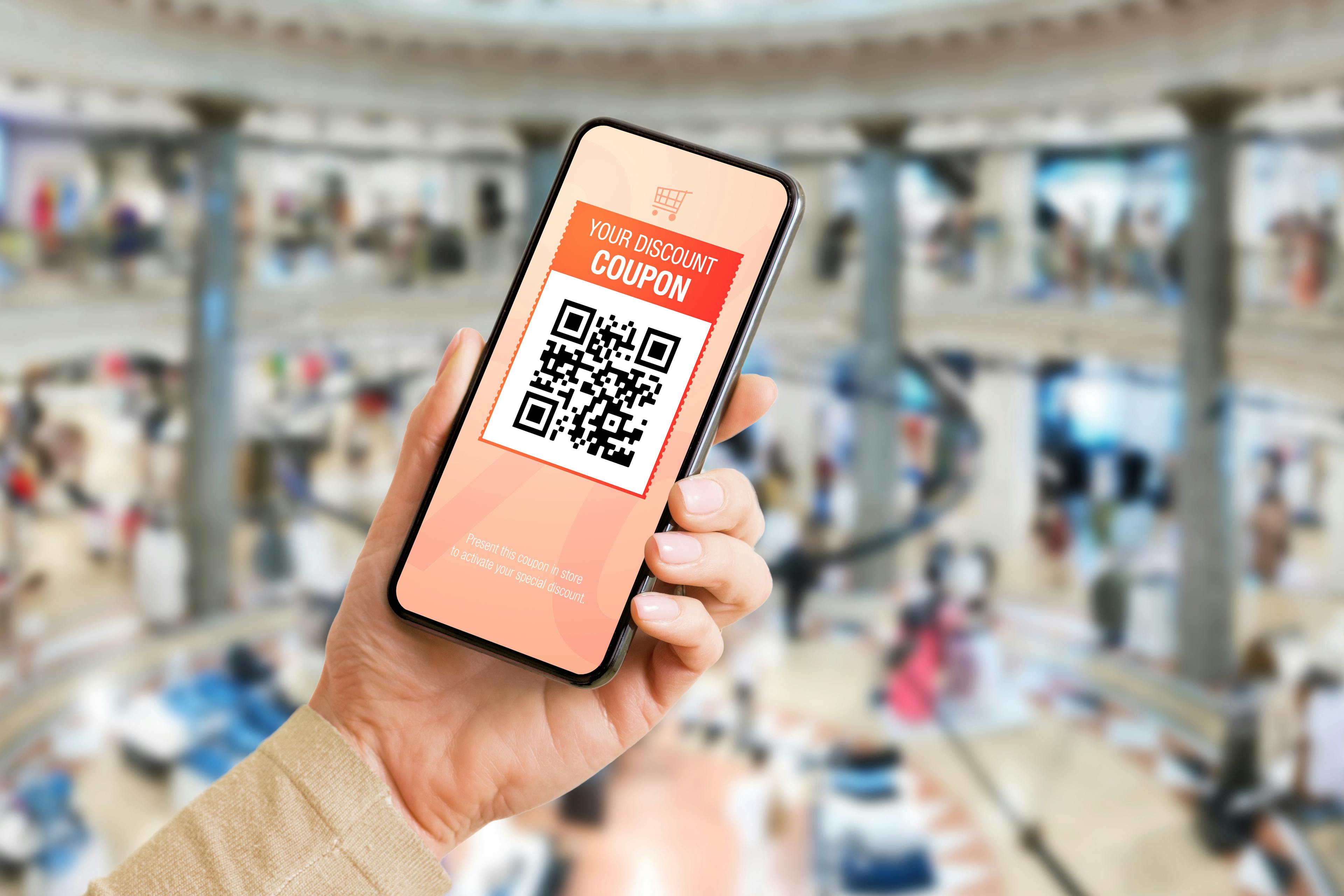 A person is holding a phone that shows a QR code with a coupon.