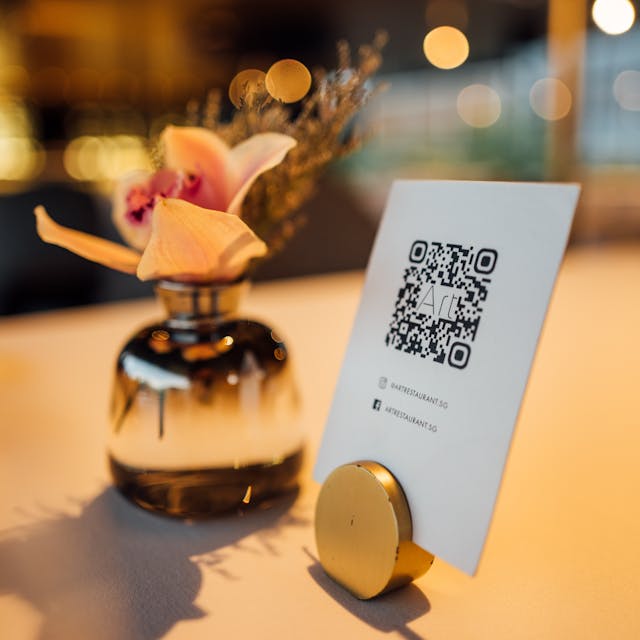 The QR code printed on a paper in a stand on the table. Flowers in the background.