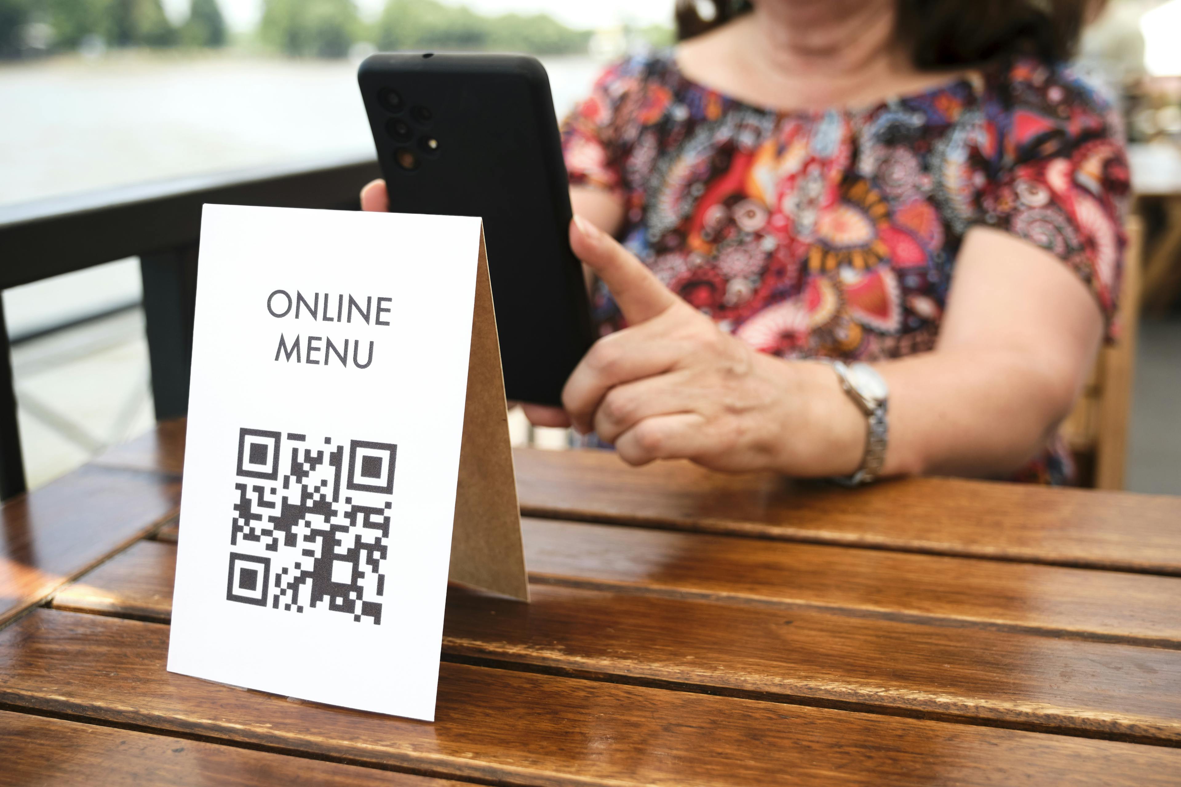 A woman sitting in a restaurant and scanning a QR code menu with her phone. The QR code redirects her to the menu.