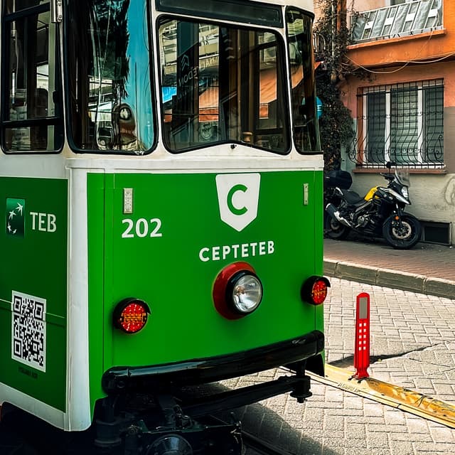 The tram with an ad on the side. The has a QR code on the corner. The code is used to let people go to the advertiser website fast when the tram is moving. The weather is good and the sun is shining.